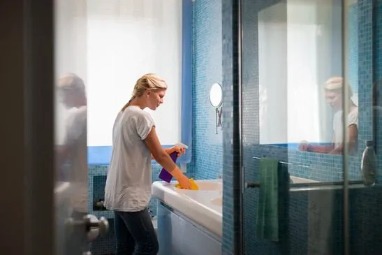 Housework and domestic lifestyle: woman doing chores in bathroom at home, cleaning wash basin and tap with spray detergent